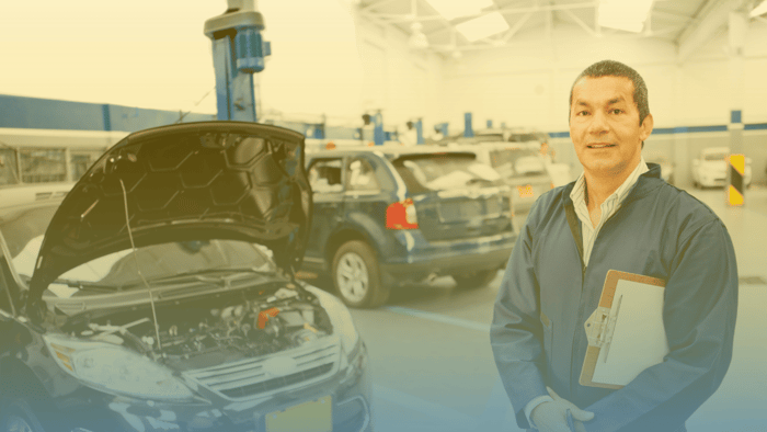 technician holding clipboard standing in a shop in front of vehicles